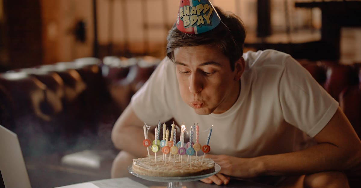 Young man blowing out candles on a birthday cake, wearing a party hat, celebrating a special occasion in a cozy indoor setting.