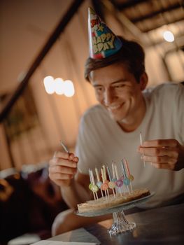 A man celebrates his birthday at home with a cake and colorful candles.