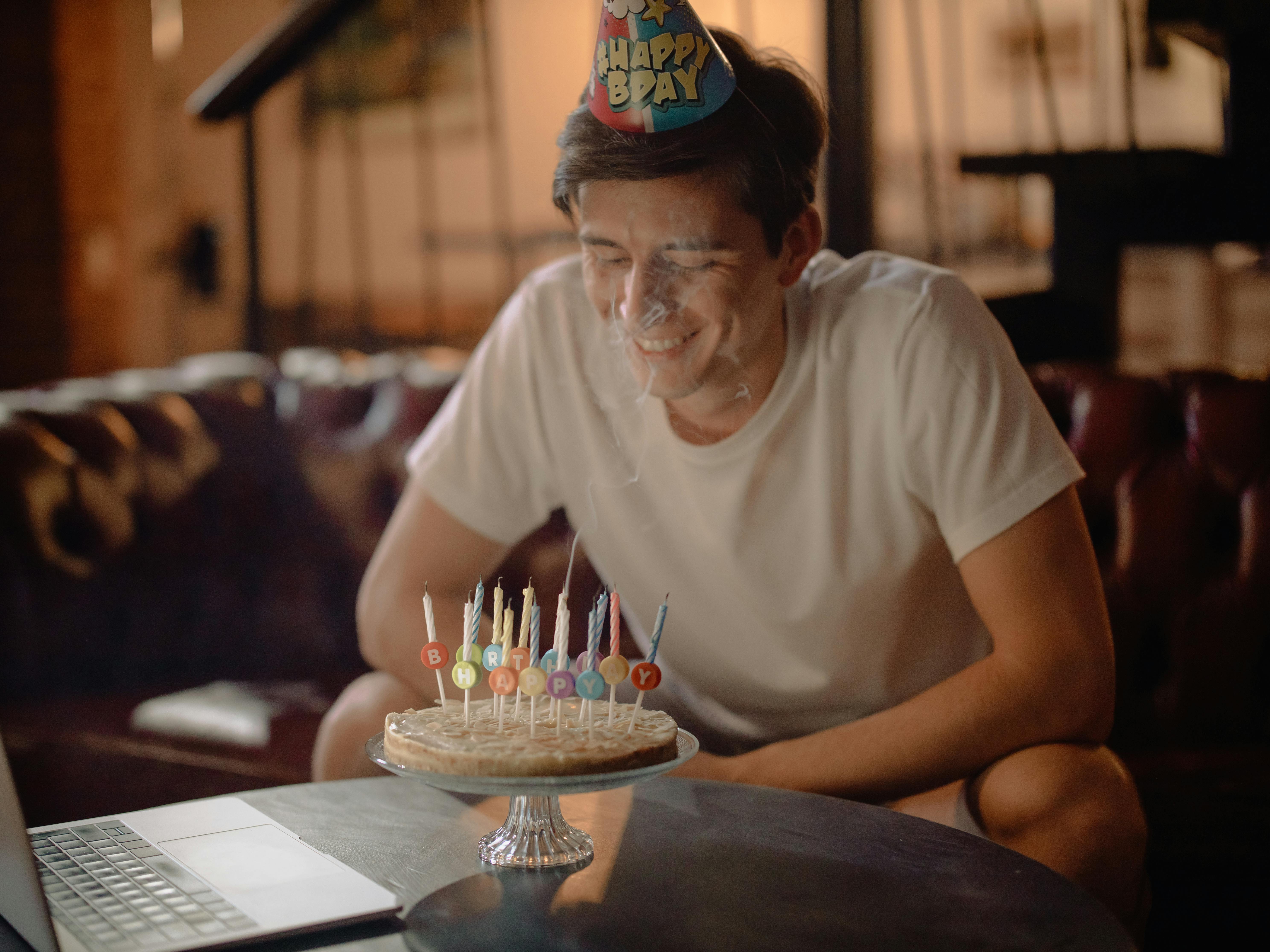 man in white crew neck t shirt sitting by the table with cake on top