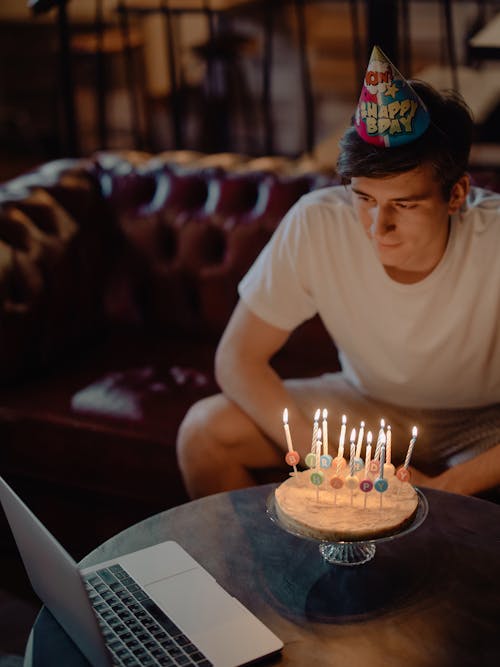 Man in White Crew Neck T-shirt Sitting on Chair in Front of Cake on Table
