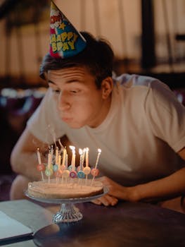 A young man blowing out candles on a birthday cake at home.