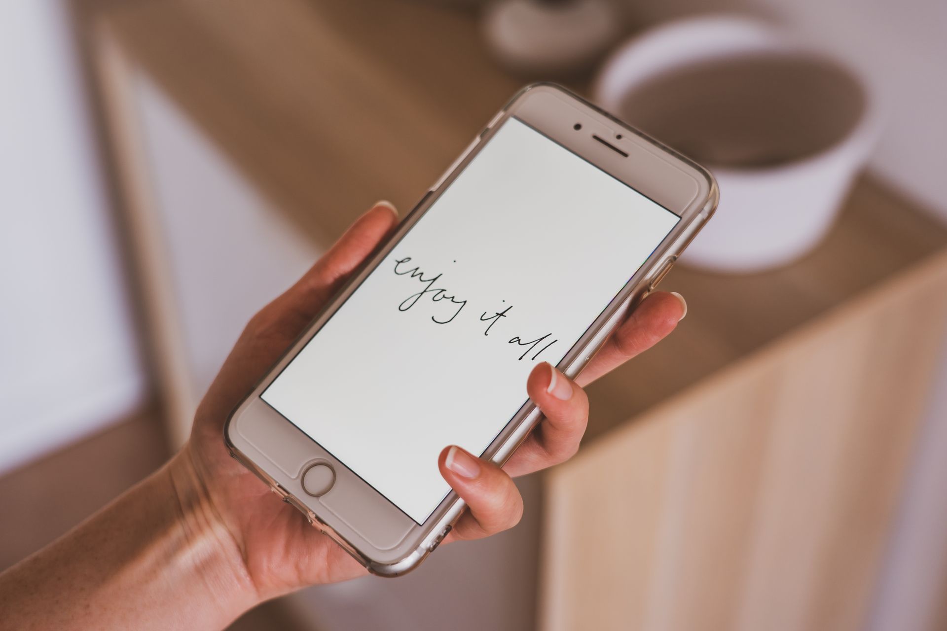 A hand holding a smartphone with an inspirational message: 'enjoy it all'.