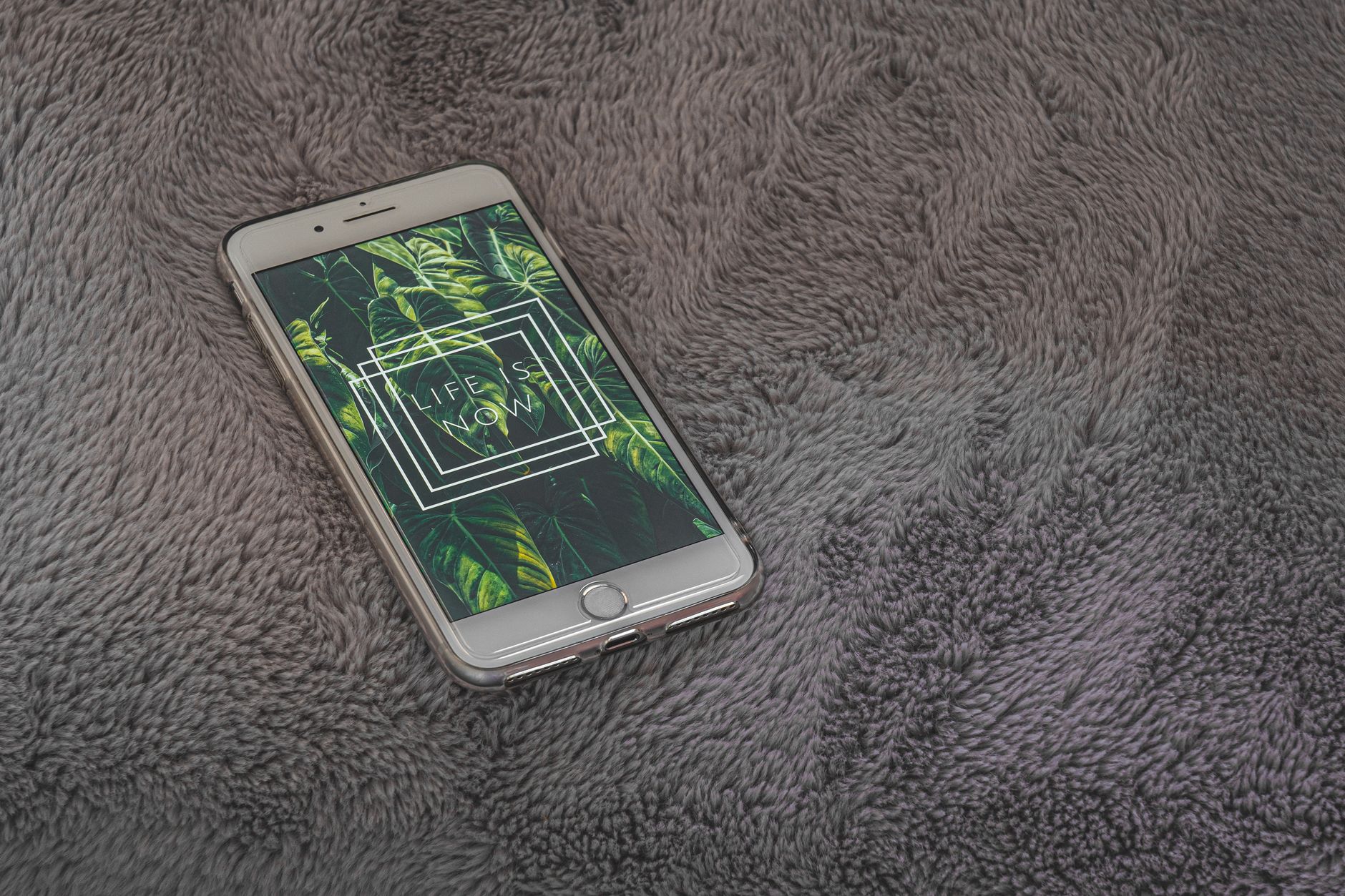 Smartphone on soft fabric with 'Life is Now' quote, highlighting technology and comfort.