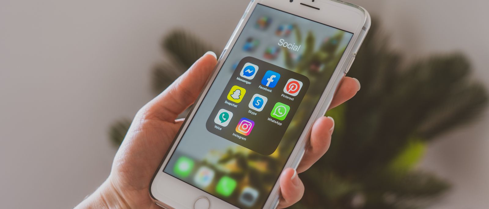 Close-up of a hand holding a smartphone displaying popular social media apps.