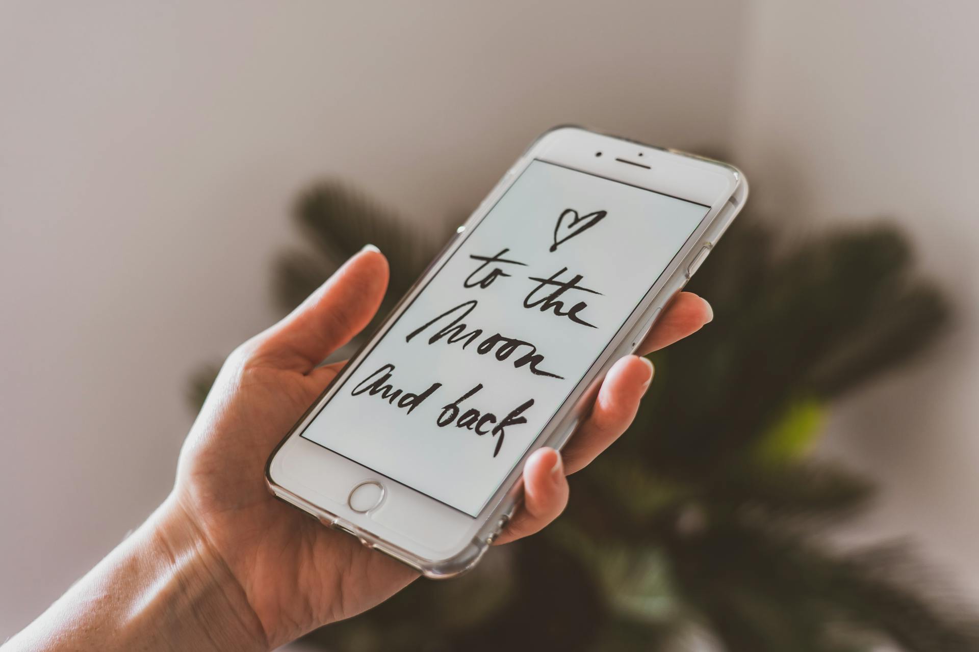 A hand holding a smartphone displaying an inspirational quote 'to the moon and back' in calligraphy.