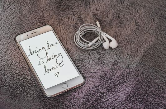Smartphone displaying motivational quote with earphones on soft fabric background.