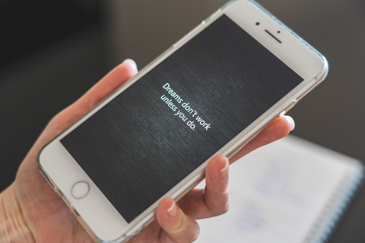 close up of hand holding smartphone with motivational quote dreams don