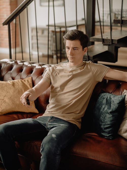 Man in Brown Polo Shirt and Blue Denim Jeans Sitting on Brown Couch