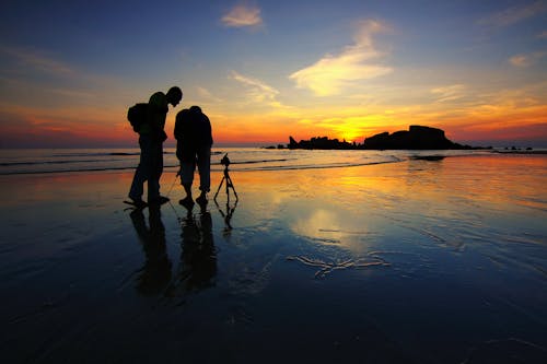 無料 ゴールデンアワーの間に海岸近くで写真を撮る二人のシルエット 写真素材