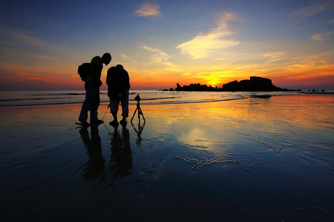 兩人在黃金時段附近海岸拍照的剪影
