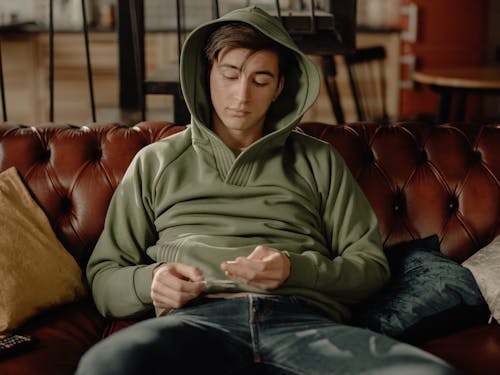 Man in Gray Hoodie Sitting on Brown Leather Couch