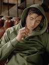一个穿着绿色连帽衫的年轻人坐在室内的真皮沙发上嚼着口香糖
