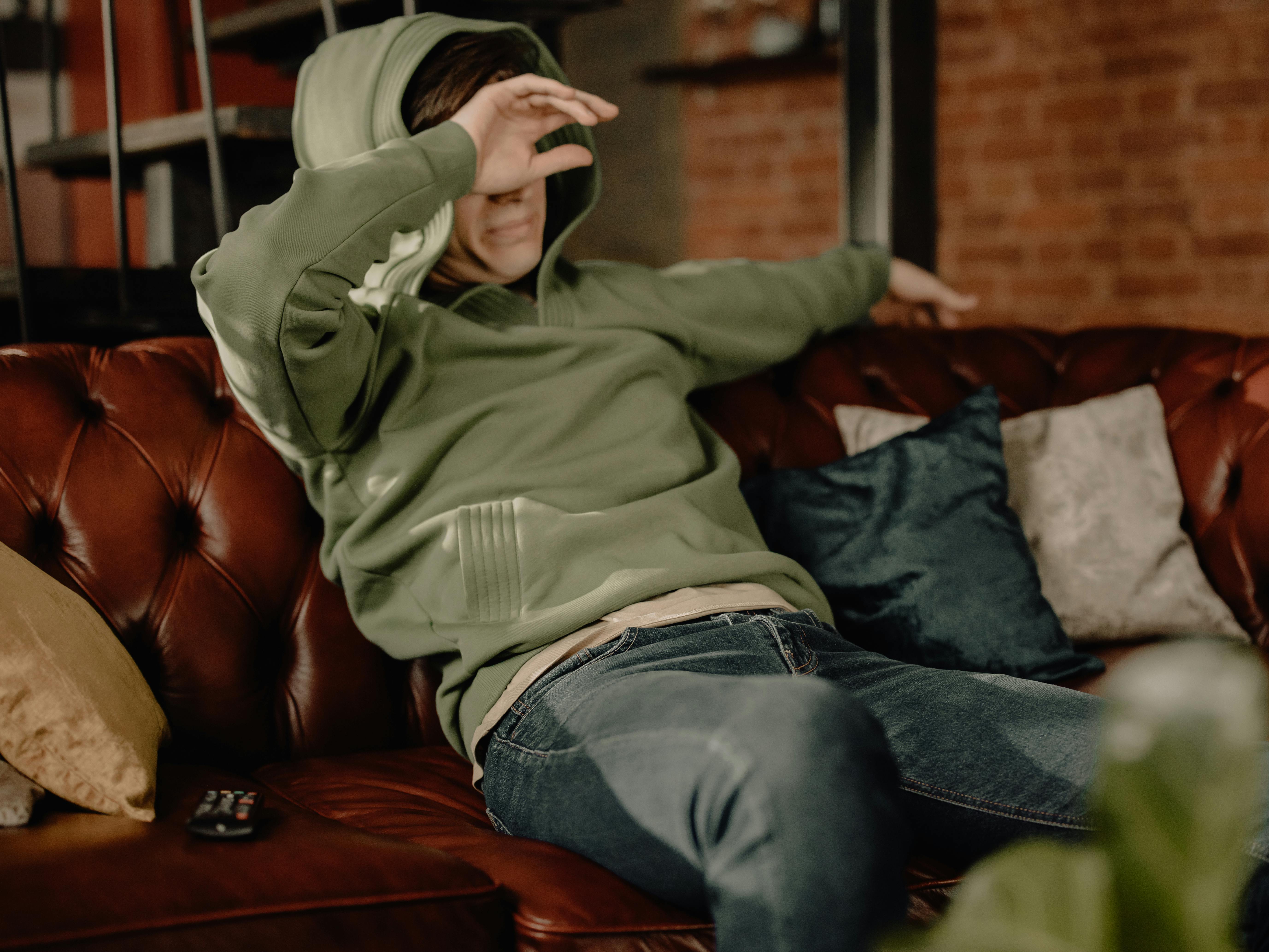 woman in gray hoodie and blue denim jeans sitting on brown leather couch