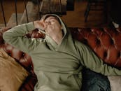 一个穿着绿色连帽衫的男人，在舒适的家庭环境中，正放松地坐在真皮沙发上