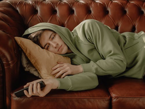 Free Man in Gray Hoodie Lying on Brown Leather Couch Stock Photo