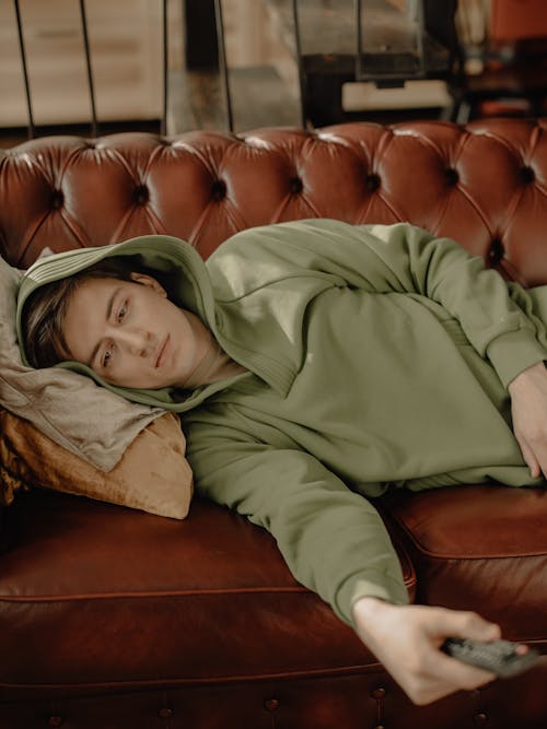 Woman in Green Hoodie Lying on Brown Leather Couch