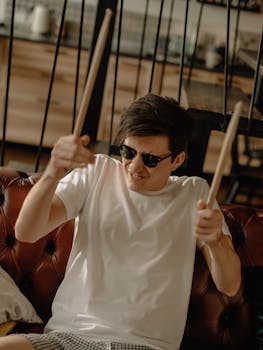 Young man in white t-shirt playing drumsticks indoors with passion.