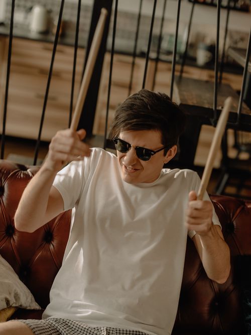Free Young man in white t-shirt playing drumsticks indoors with passion. Stock Photo