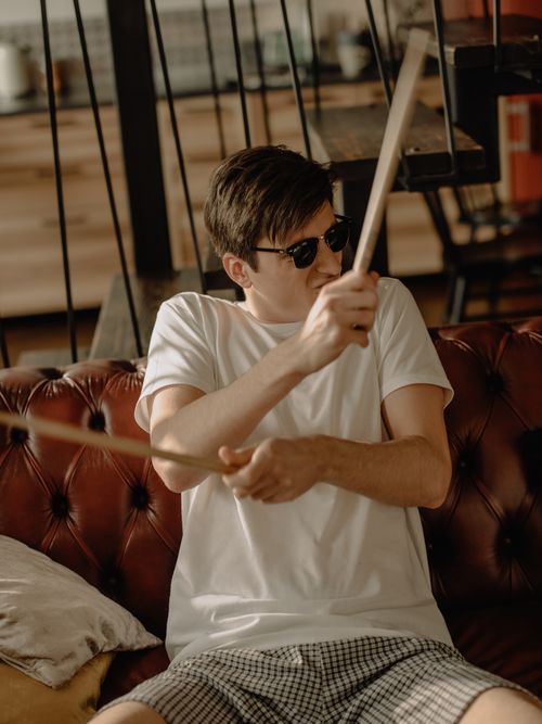 Free Young man wearing sunglasses playing air drums on a leather sofa at home. Stock Photo
