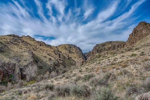 Scenery view of blue sky with clouds above mountains covered with dry grass and bushes