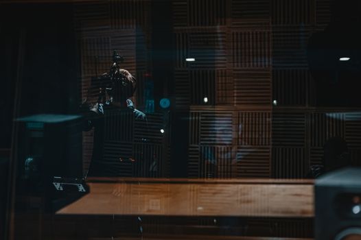 Faceless man in casual clothing taking video while male colleague working with equipment in recording studio