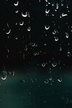 A detailed view of raindrops on a window, creating a moody and serene night atmosphere.