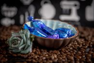 A decorative bowl with wrapped candies surrounded by coffee beans and a flower.