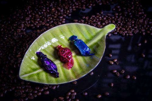 Free Vibrant candies wrapped in foil on a leaf-shaped dish surrounded by coffee beans. Stock Photo