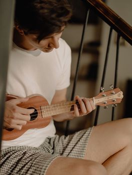 A man playing a ukulele in a cozy home environment, wearing casual clothing.