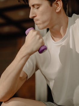 Focused young man lifting a dumbbell at home. Achieving fitness goals indoors.