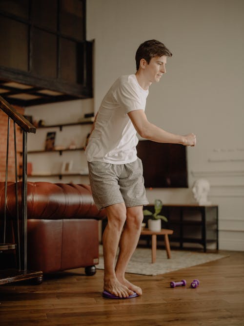 Free Woman in White T-shirt and Gray Skirt Standing on Brown Wooden Floor Stock Photo