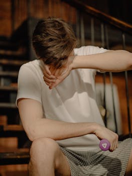 A man in casual clothes with a dumbbell relaxing on stairs indoors.