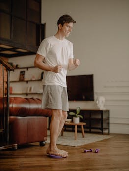 Man in casual attire exercising at home with minimal equipment.
