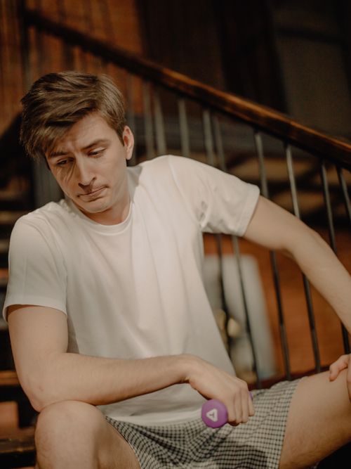 Free Young man at home in casual attire holding a dumbbell on stairs. Stock Photo