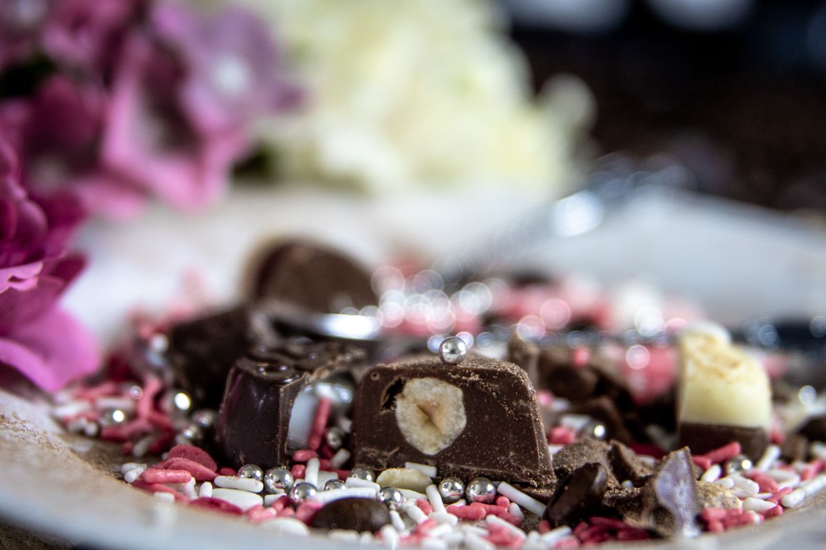 Delightful close-up of assorted chocolate candies surrounded by colorful sprinkles and blurred floral background.