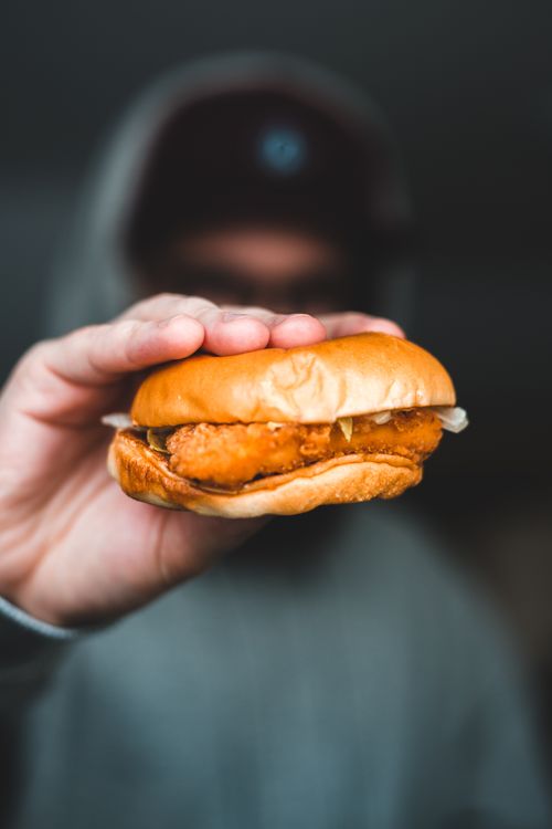 Free Selective focus of male in grey hoodie and hat showing burger with chicken cutlet Stock Photo