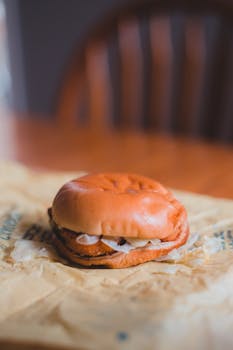 Appetizing small burger with slices of onion and fried cutlet between round buns on wooden table on blurred background