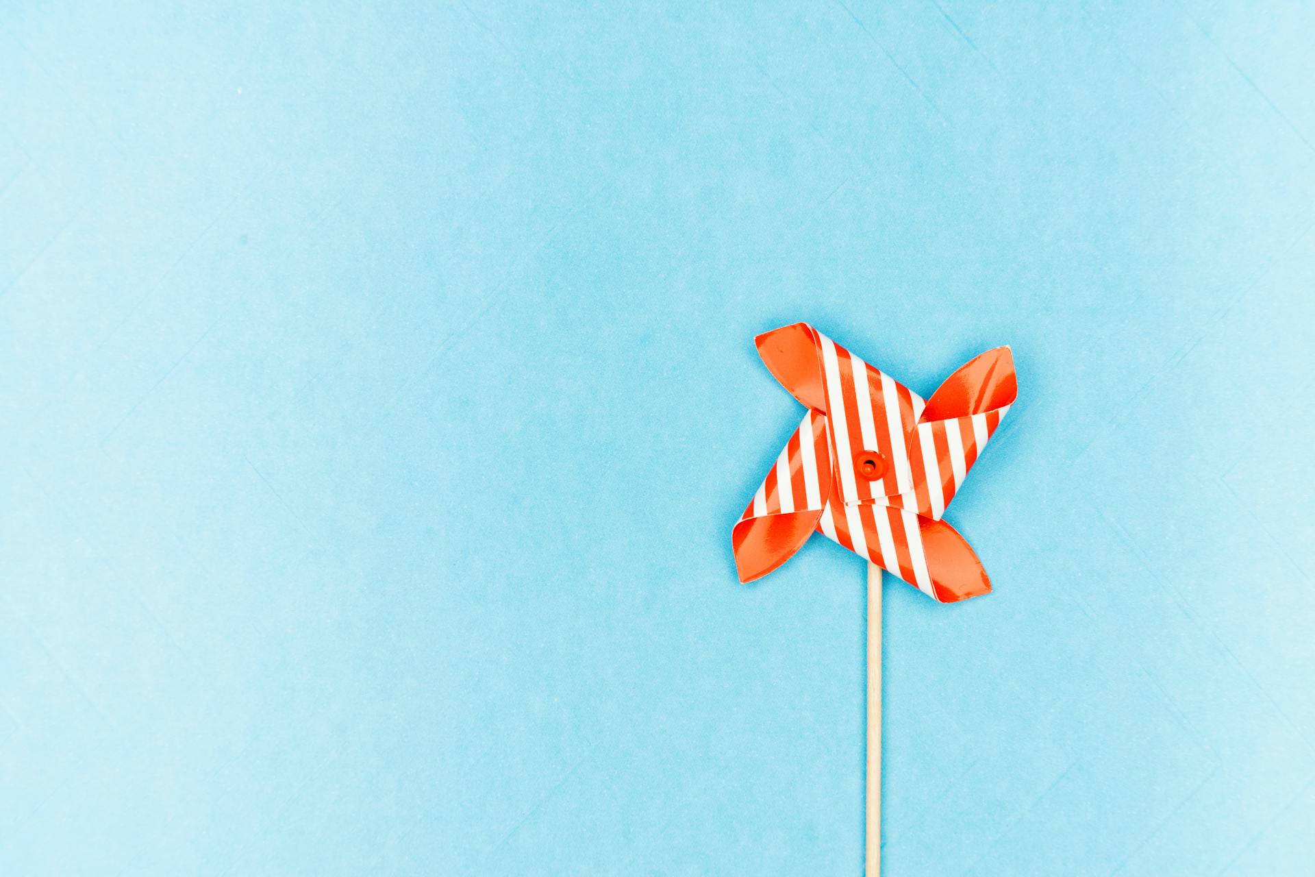 Bright orange pinwheel toy on a blue backdrop, perfect for playful concepts.