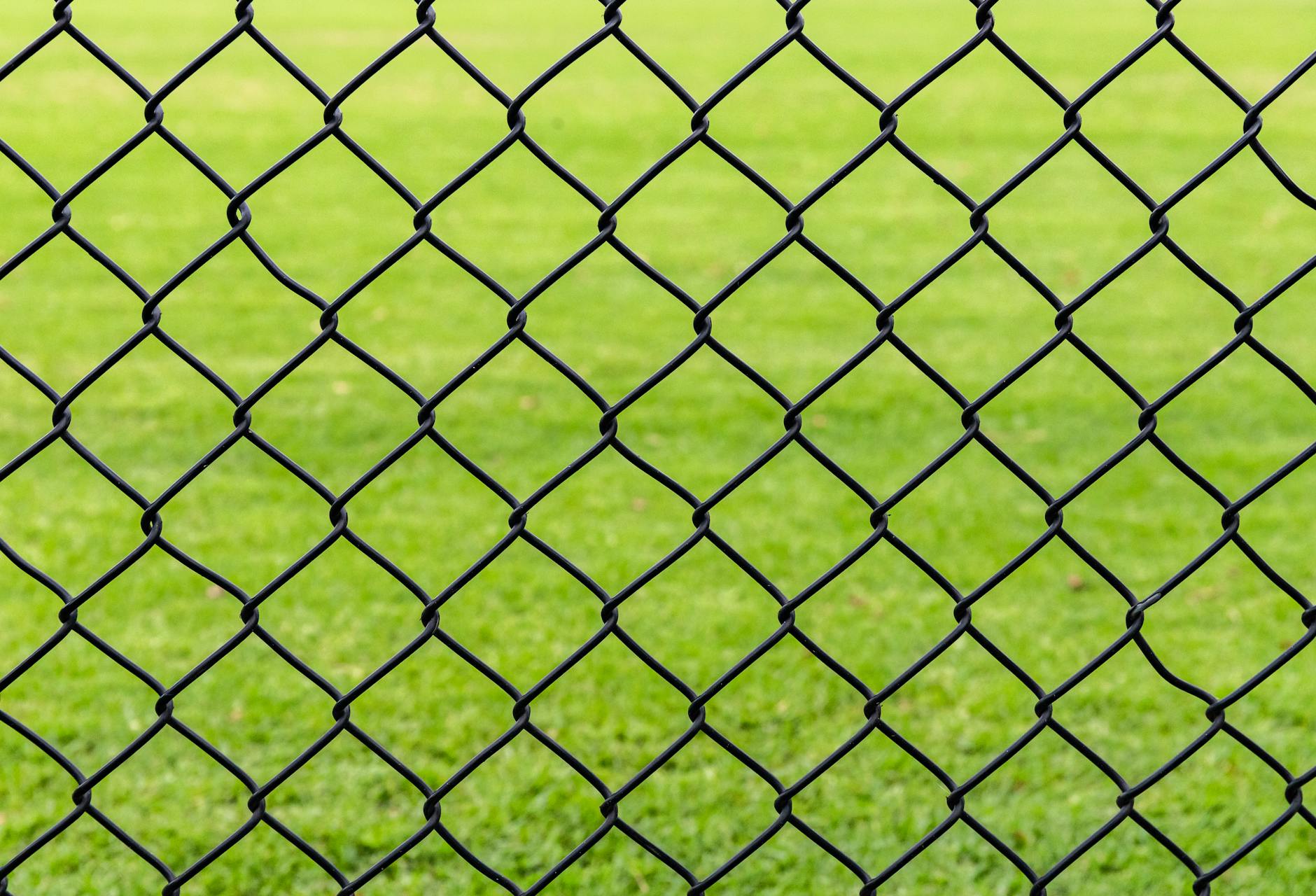 Full frame background of fence with chain link net on blurred green meadow