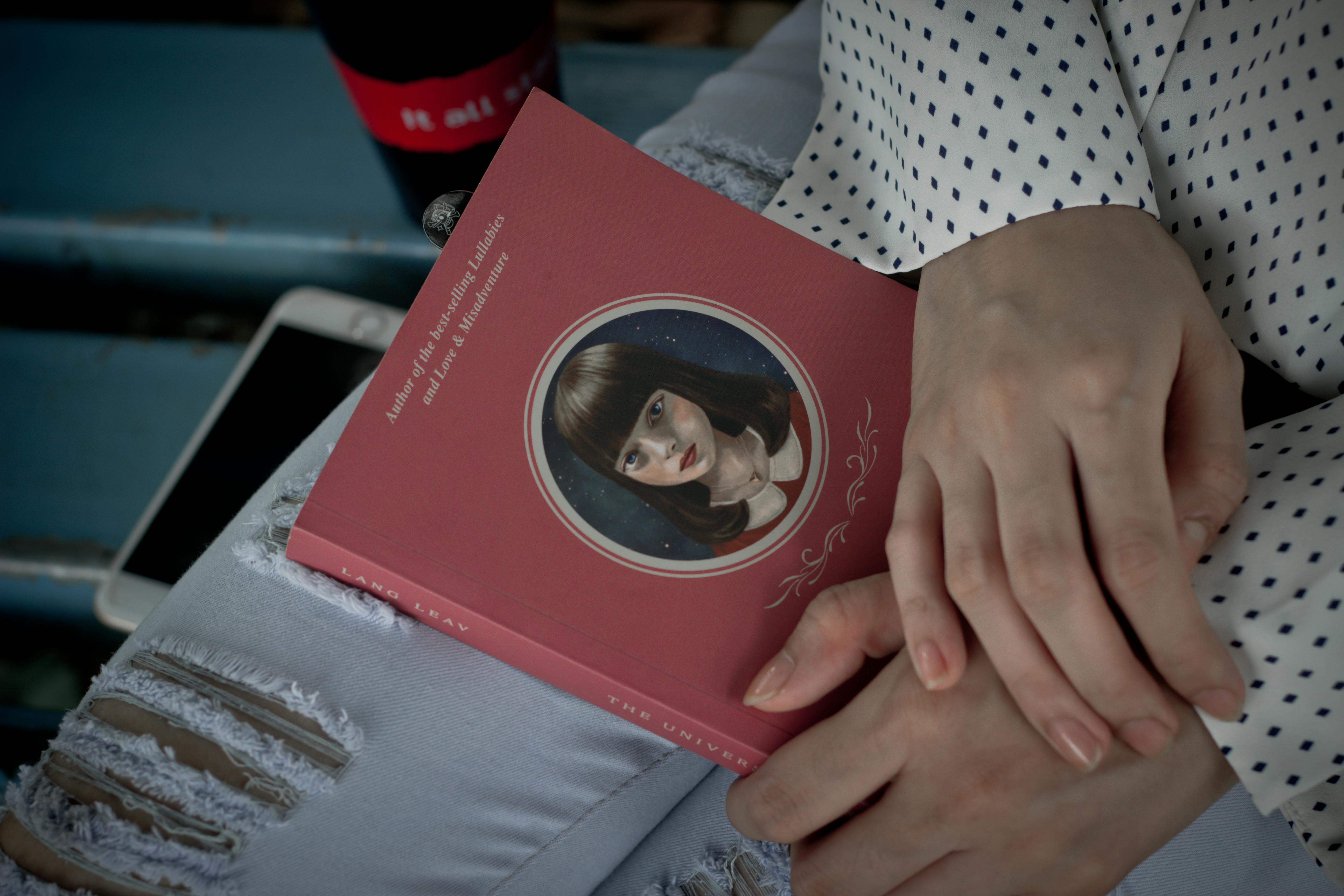 A woman in a polka dot shirt holds a novel in a serene setting, ideal for leisure reading.