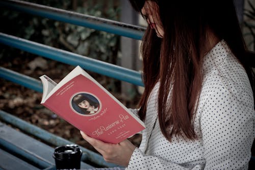 Woman Sitting on a Bench, Drinking Coffee and Reading a Book