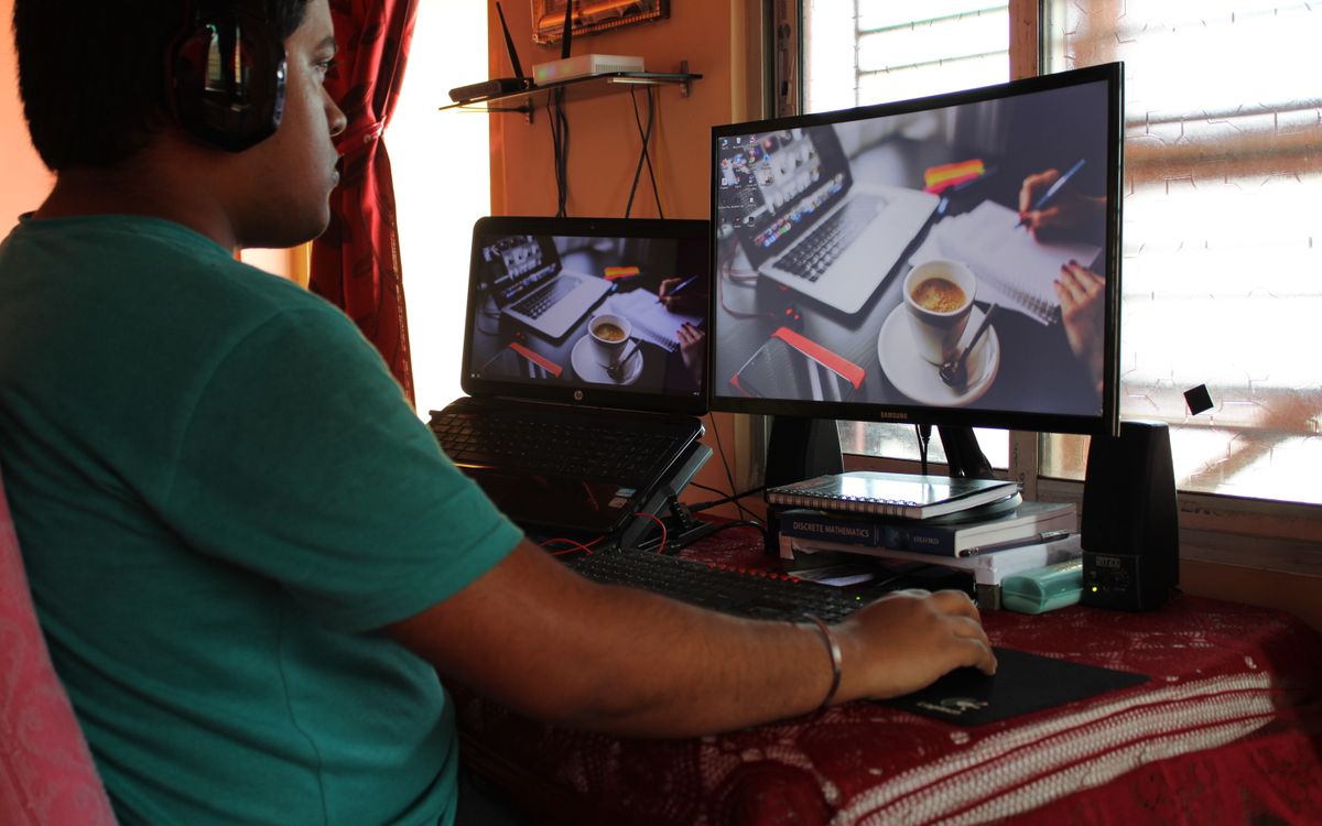 A person working from home in Kolkata with dual monitors, coffee, and headphones. Ideal for remote work concepts.