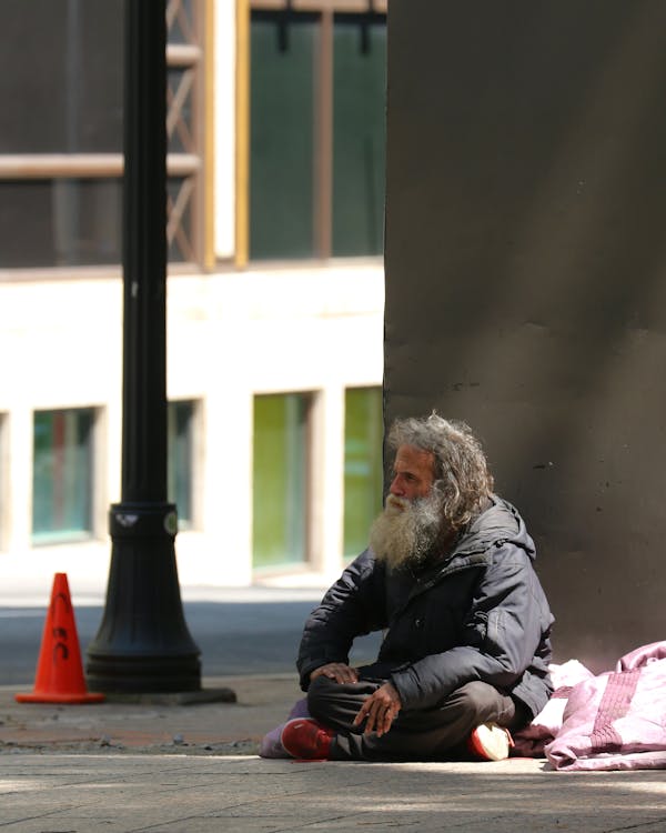 Man in Black Jacket Sitting on Sidewalk