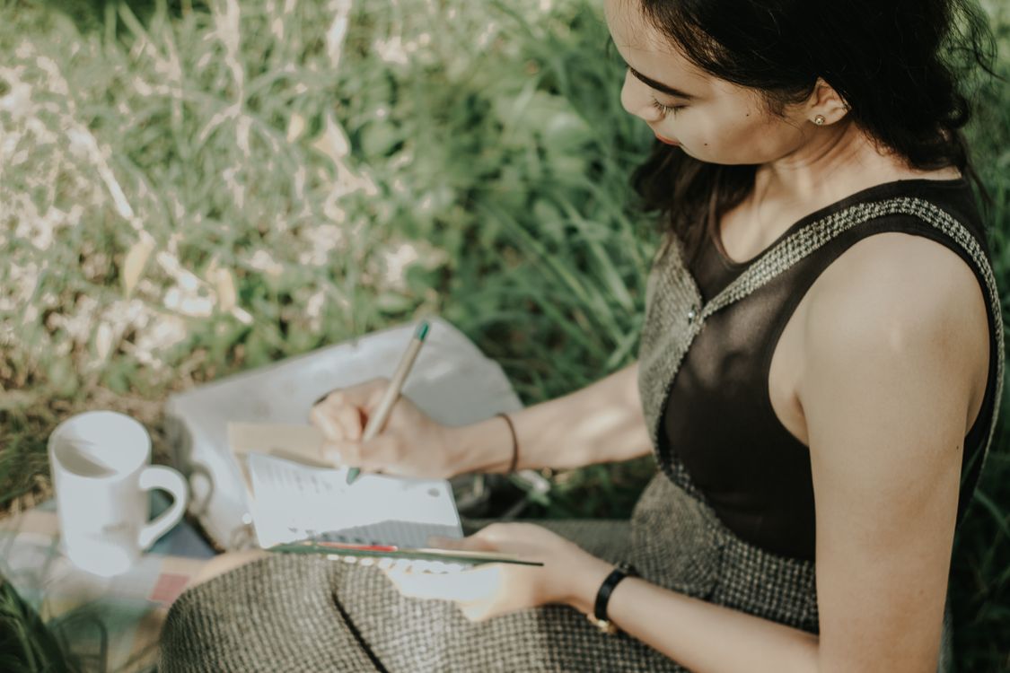 Young mother journaling outdoors, pen in hand, taking a peaceful pause
