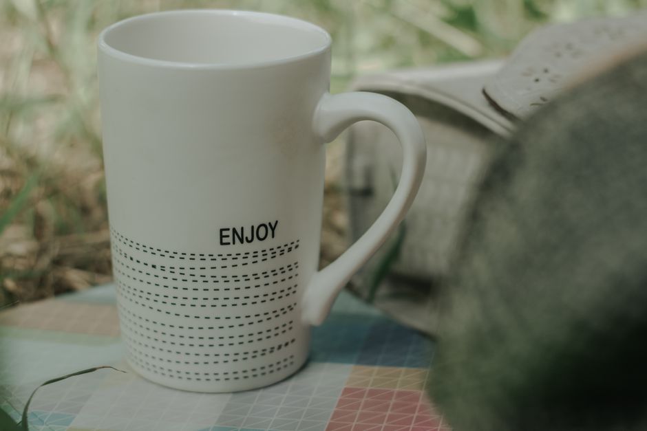 A minimalist white mug with 'Enjoy' print, placed outdoors on a table, creating a calm scene.