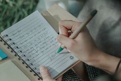 A woman's hand writing in a notebook, capturing thoughts on paper outdoors.