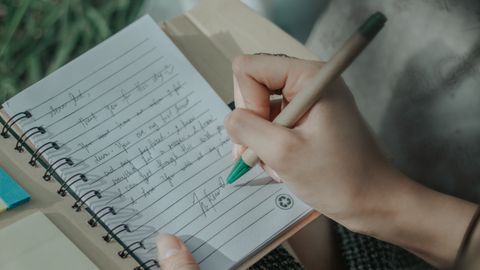 A woman's hand writing in a notebook, capturing thoughts on paper outdoors.