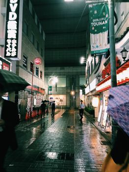 新宿潮湿的夜景中，充满活力的灯光映照在人行道上