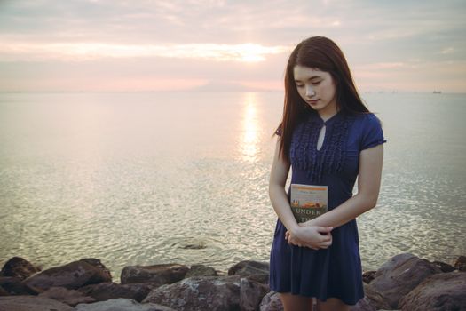 Peaceful moment of a woman holding a book at the Calabarzon seashore during sunset.
