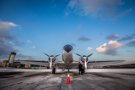 A classic propeller airplane parked on the tarmac at Amman Airport under a blue sky.